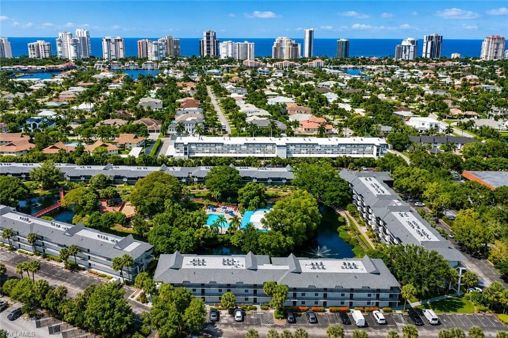 Aerial overview of a coastal community featuring multi-story residential buildings with gray roofs, surrounded by lush green landscaping and mature trees