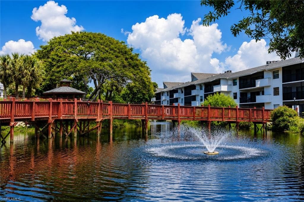 Community pond with a central fountain, bordered by a wooden pedestrian bridge with red railings