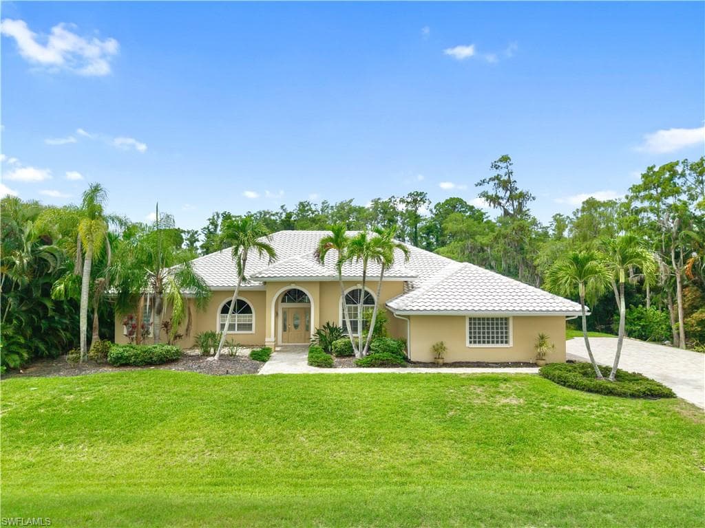 Front elevation featuring a new tile roof, paver driveway, mature tropical landscaping, and oversized garage, ideally situated on one of Fiddlesticks Country Club's most private golf course homesites.