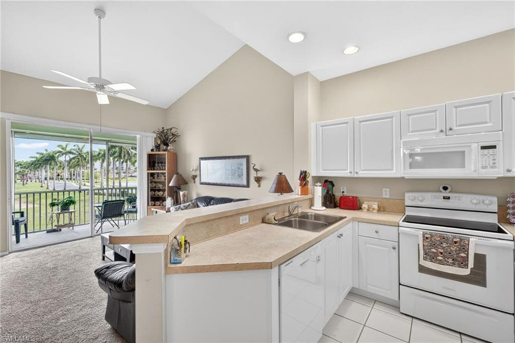 Open-concept kitchen with white cabinetry and a double basin sink, featuring a breakfast bar with a neutral countertop