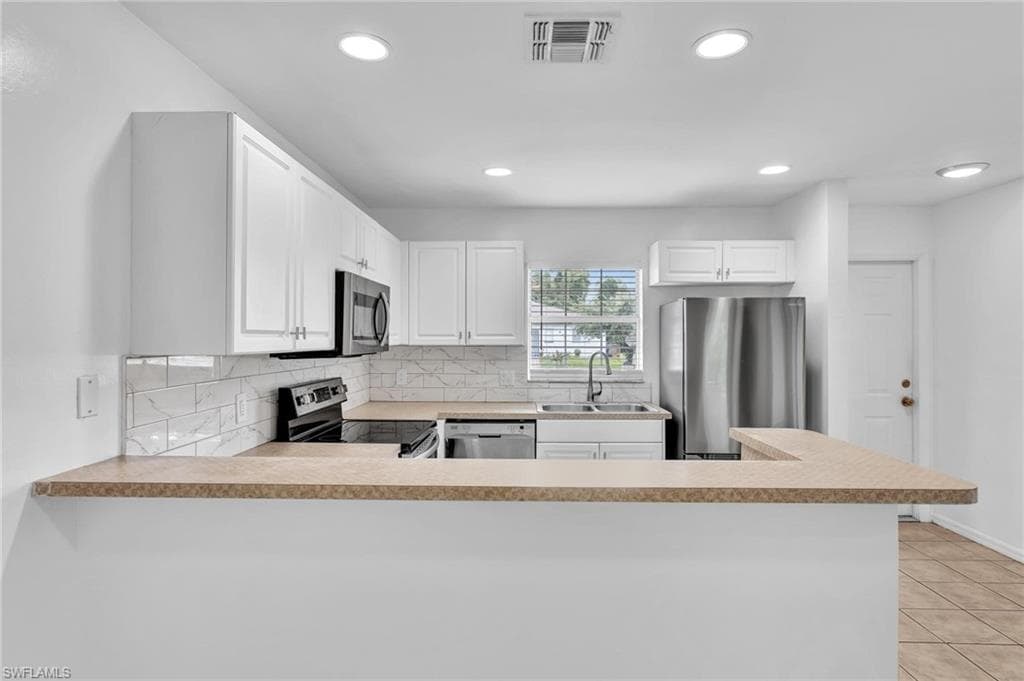 Kitchen featuring white cabinetry, light-toned countertops, a white subway tile backsplash, and stainless steel appliances