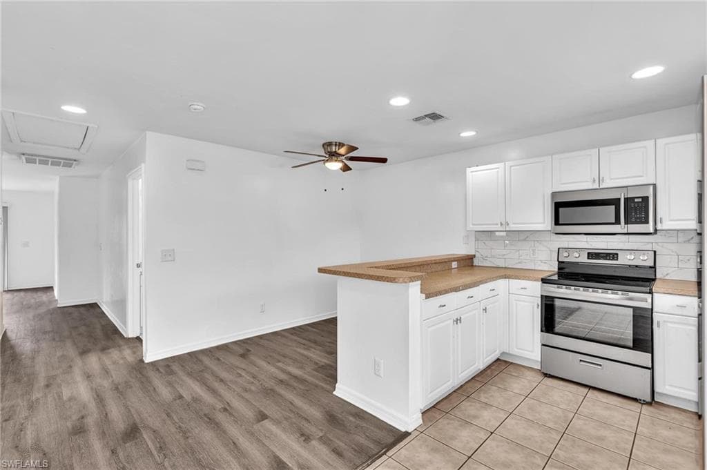 Open-concept kitchen with white cabinetry, stainless steel appliances, and a breakfast bar