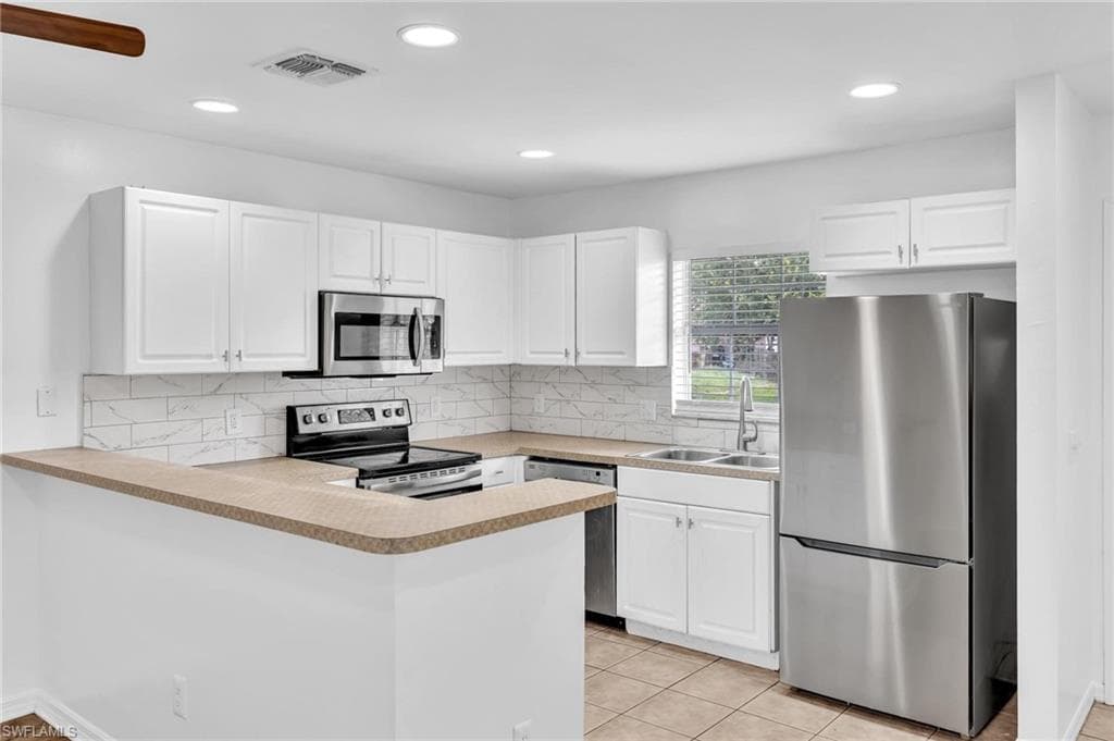 Modern kitchen featuring white cabinetry, light countertops, stainless steel appliances, and a tiled backsplash