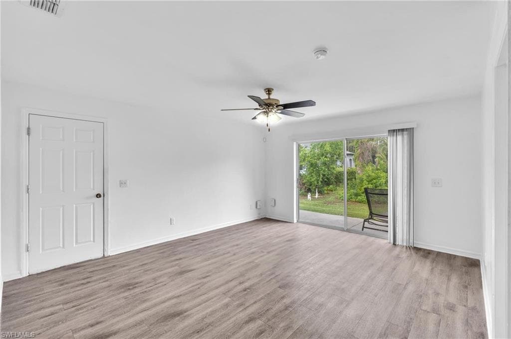 Open-concept room featuring wood-finish flooring, a ceiling fan with integrated lighting, and a white paneled door