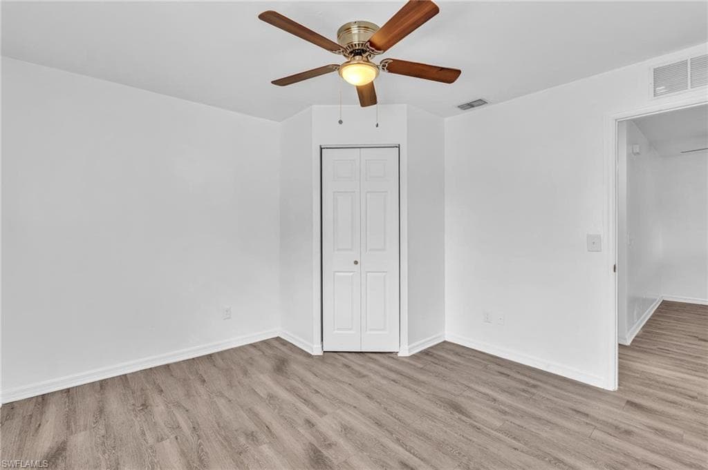 Bright room featuring wood-finish flooring, a bi-fold closet door, and a ceiling fan with integrated lighting