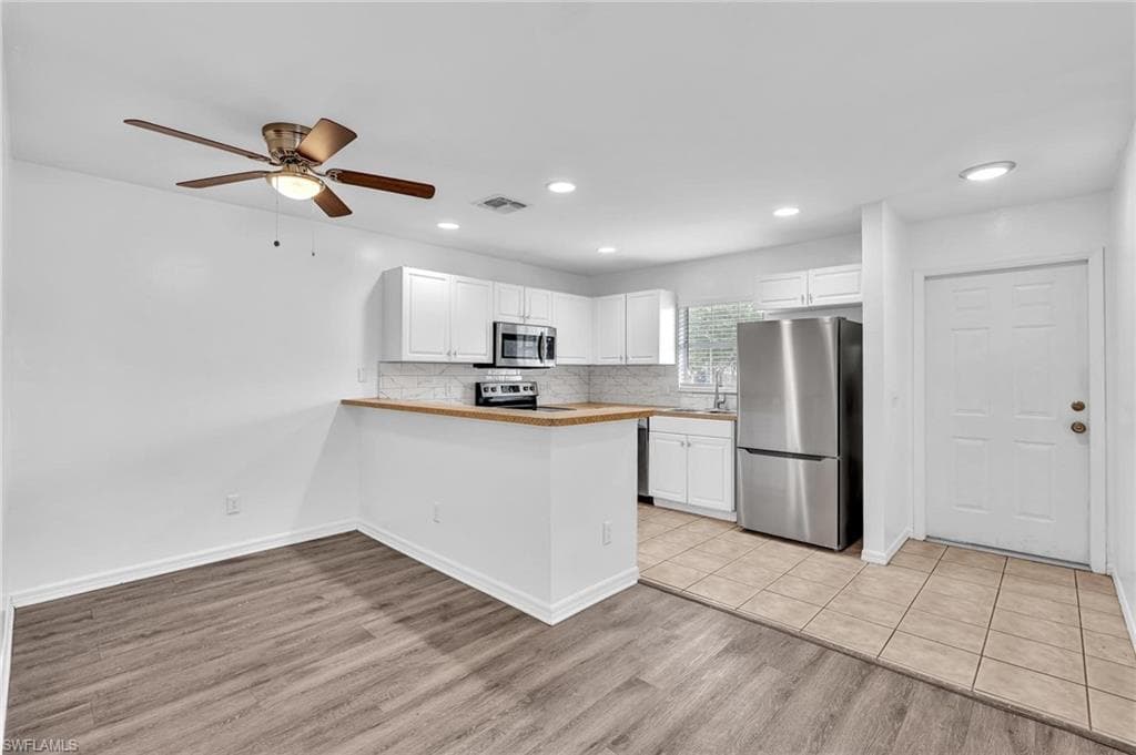 Bright kitchen featuring white cabinetry, stainless steel appliances, and wood-finish countertops