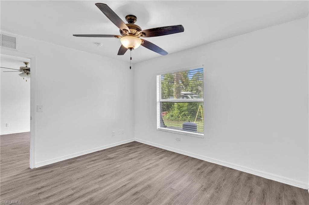Spacious room featuring wood-finish flooring, a ceiling fan with integrated lighting, and a window with horizontal blinds