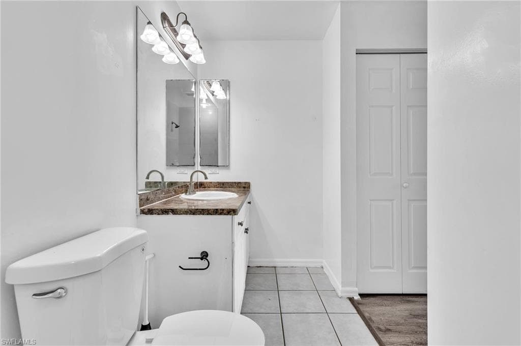 Bathroom featuring a white ceramic toilet, a vanity with a stone-finish countertop and integrated sink, a rectangular mirror, and a five-light vanity fixture