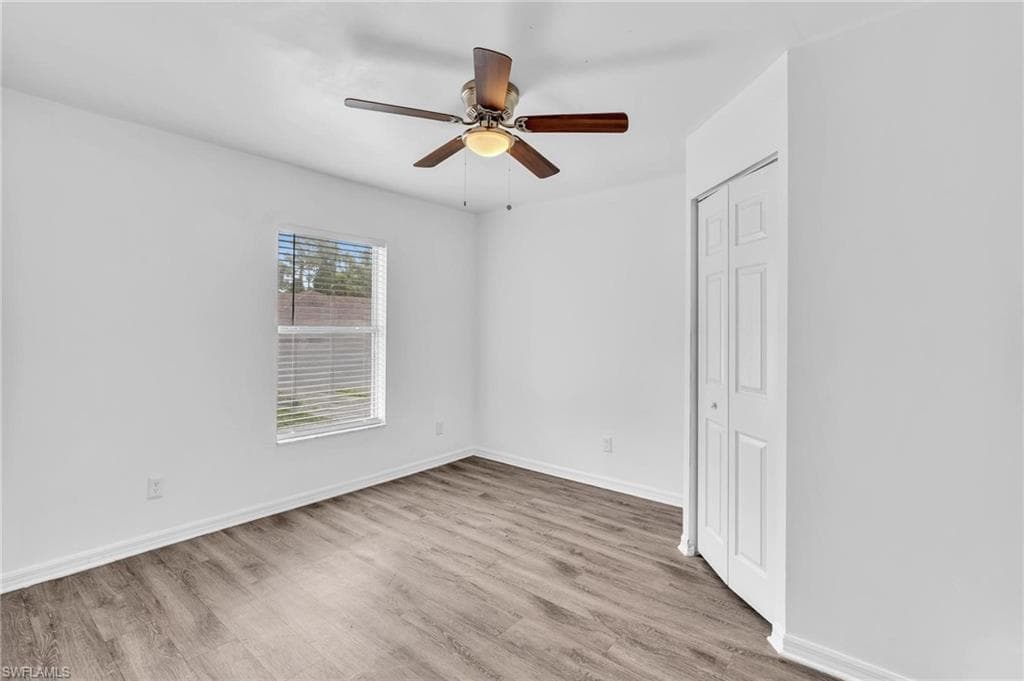 Neutral interior space featuring wood-finish flooring and a bright window with horizontal blinds