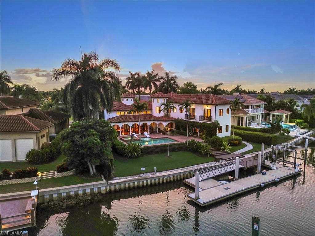 Mediterranean-style residence featuring a terracotta tile roof, white stucco exterior, arched covered patio, private swimming pool, and a multi-slip dock with a boat lift