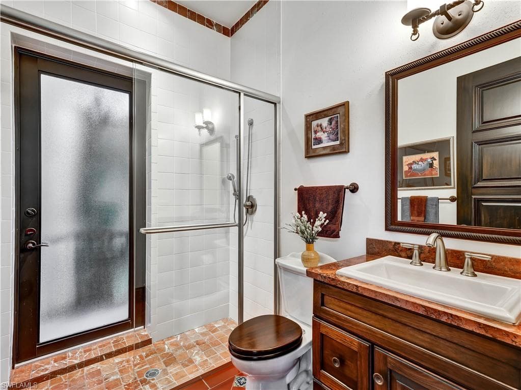 Bathroom featuring a glass-enclosed shower, wood-finish vanity with an integrated sink, stone countertop, brushed nickel fixtures, and decorative tile flooring