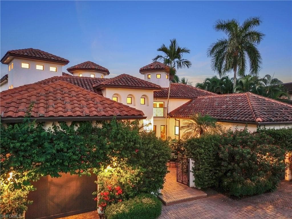 Mediterranean-inspired exterior featuring a multi-level design, red barrel tile roofing, multiple turret-style elements with square windows, and a paver driveway