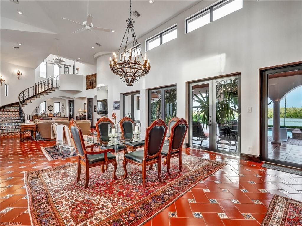 Spacious interior featuring a large dining area with a wrought iron chandelier, terracotta-style flooring with decorative tile accents, and multiple glass French doors