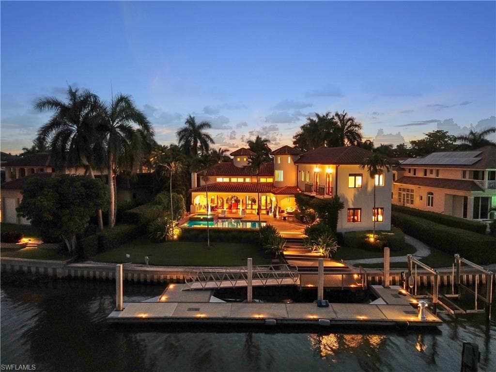 Mediterranean-style residence featuring a terracotta tile roof, private swimming pool, waterfront access with a substantial dock, integrated boat lifts, and mature palm landscaping