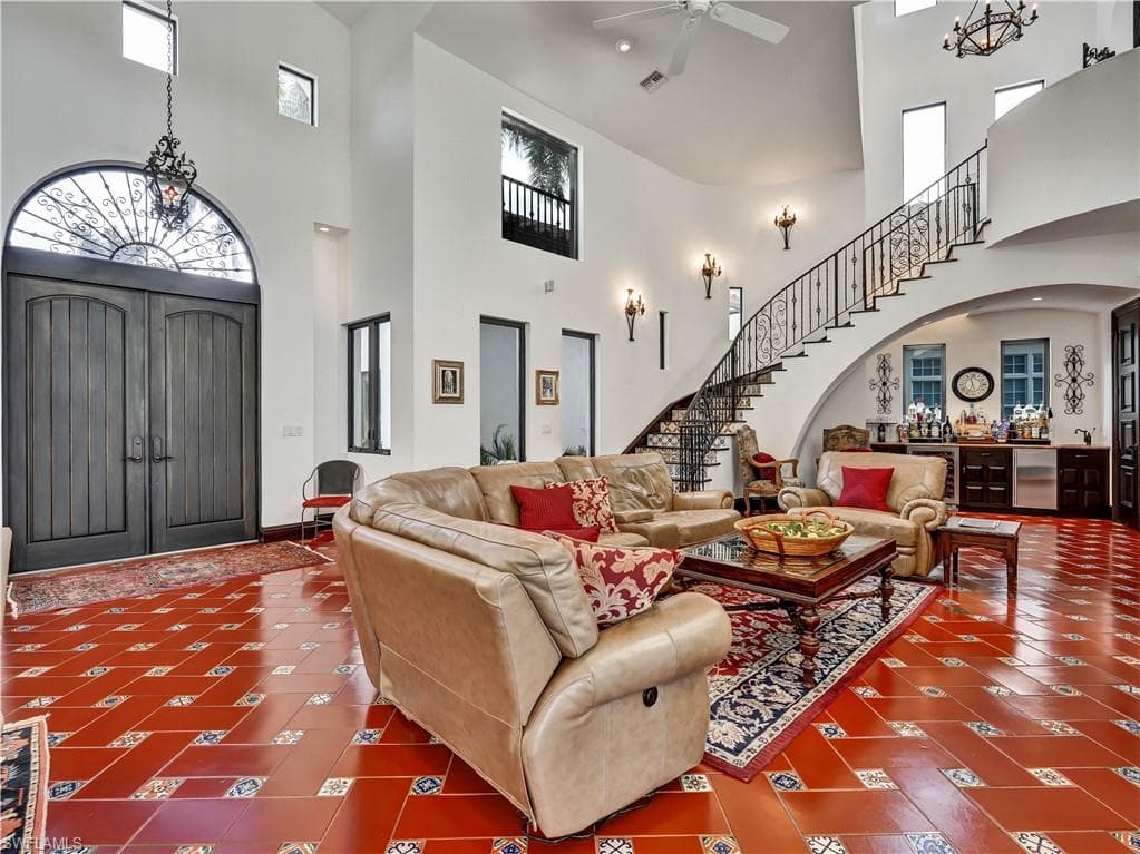 Vaulted entry foyer featuring a grand staircase with wrought iron railing, arched double doors with an ornate transom, and a built-in wet bar