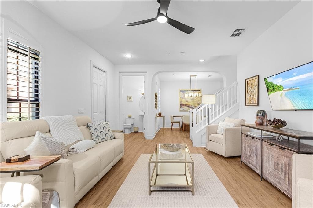 Living area with ceiling fan, light wood-style flooring, arched walkways, stairs, and a chandelier