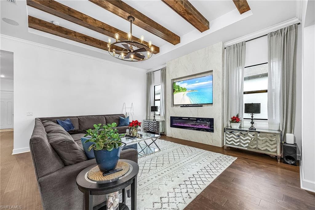 Living area with beam ceiling, dark wood-style flooring, a glass covered fireplace, hanging lights, and crown molding