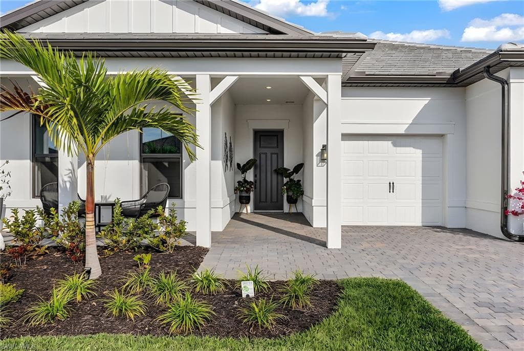 View of exterior entry with board and batten siding, decorative driveway, a garage, and stucco siding