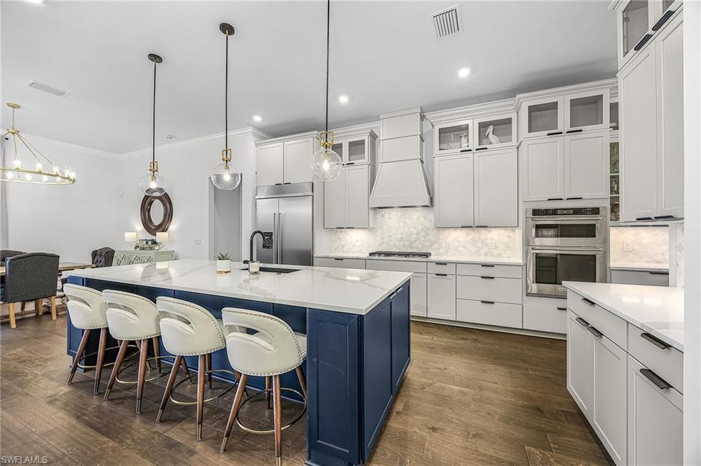 Dual tone kitchen with a breakfast bar, a kitchen island with sink, dark wood finished floors, backsplash, and ornamental molding