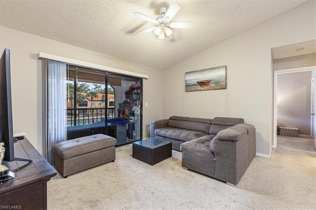 Living room featuring lofted ceiling, light colored carpet, a textured ceiling, and a ceiling fan