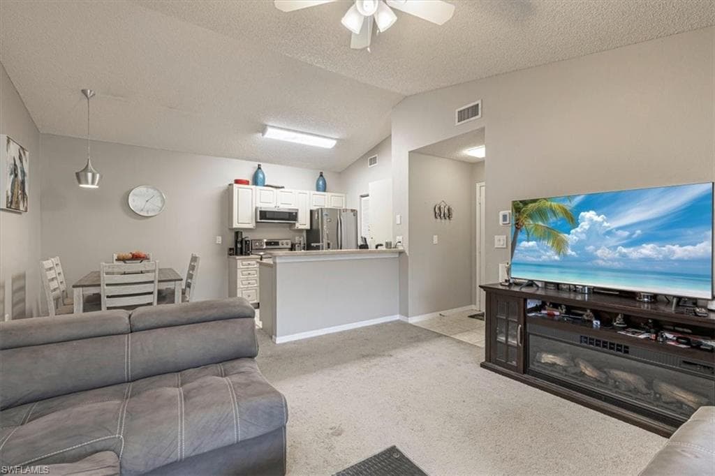 Living area featuring lofted ceiling, light colored carpet, a textured ceiling, and ceiling fan