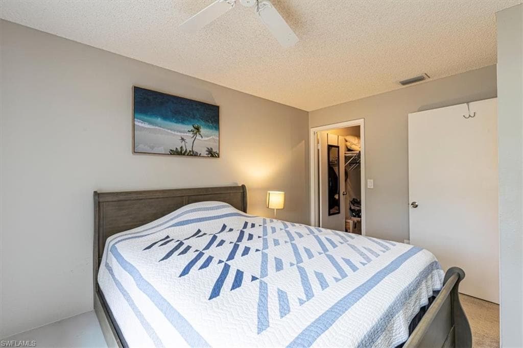 Bedroom with a walk in closet, a textured ceiling, and a ceiling fan