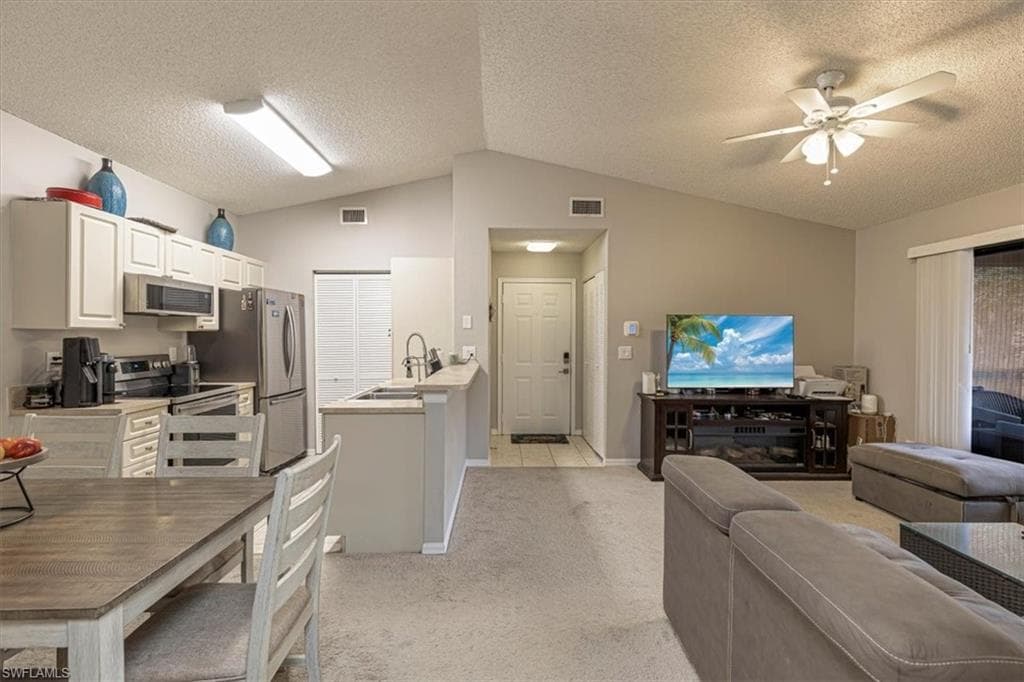 Kitchen featuring open floor plan, stainless steel appliances, light carpet, white cabinets, and vaulted ceiling