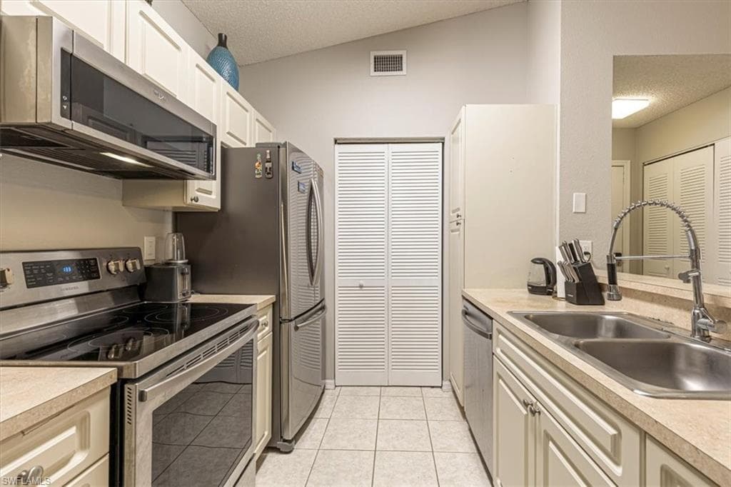 Kitchen with stainless steel appliances, light countertops, a textured ceiling, light tile patterned flooring, and lofted ceiling