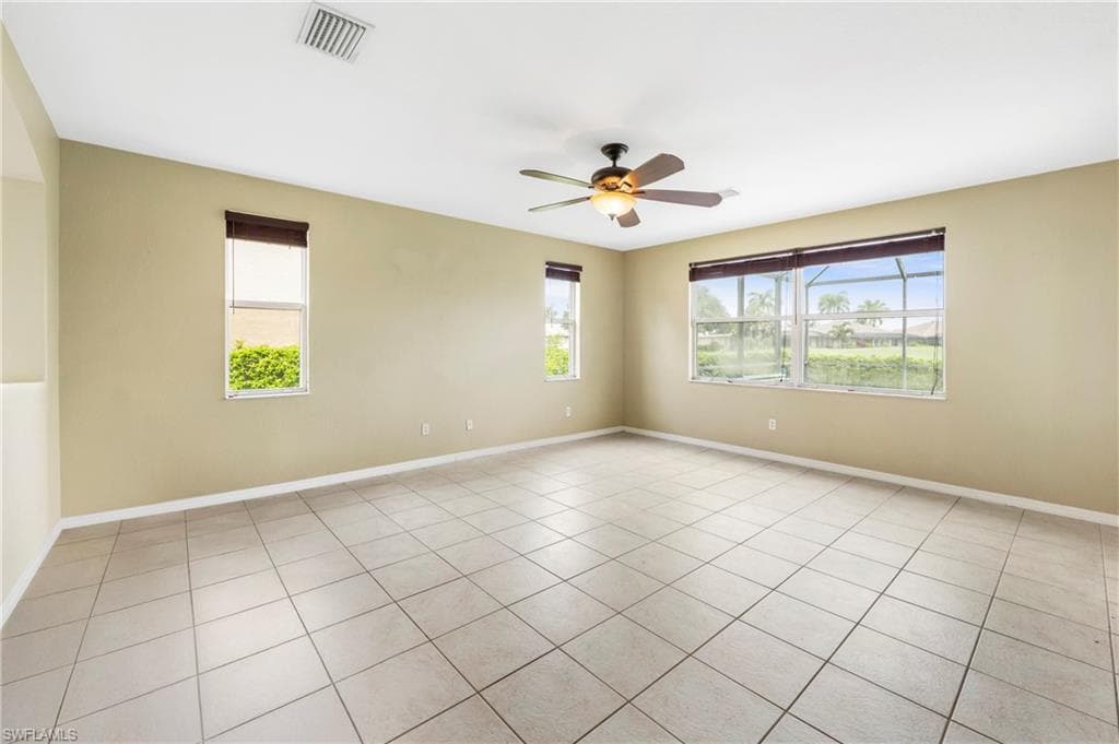 Spacious interior room featuring light-toned tile flooring, multiple windows providing natural illumination, and a ceiling fan with integrated lighting