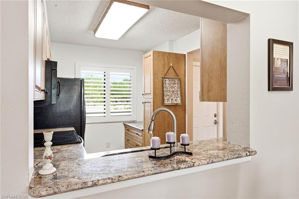 Kitchen featuring a pass-through window with granite-finish countertops, wood cabinetry, a stainless steel faucet, and a black refrigerator