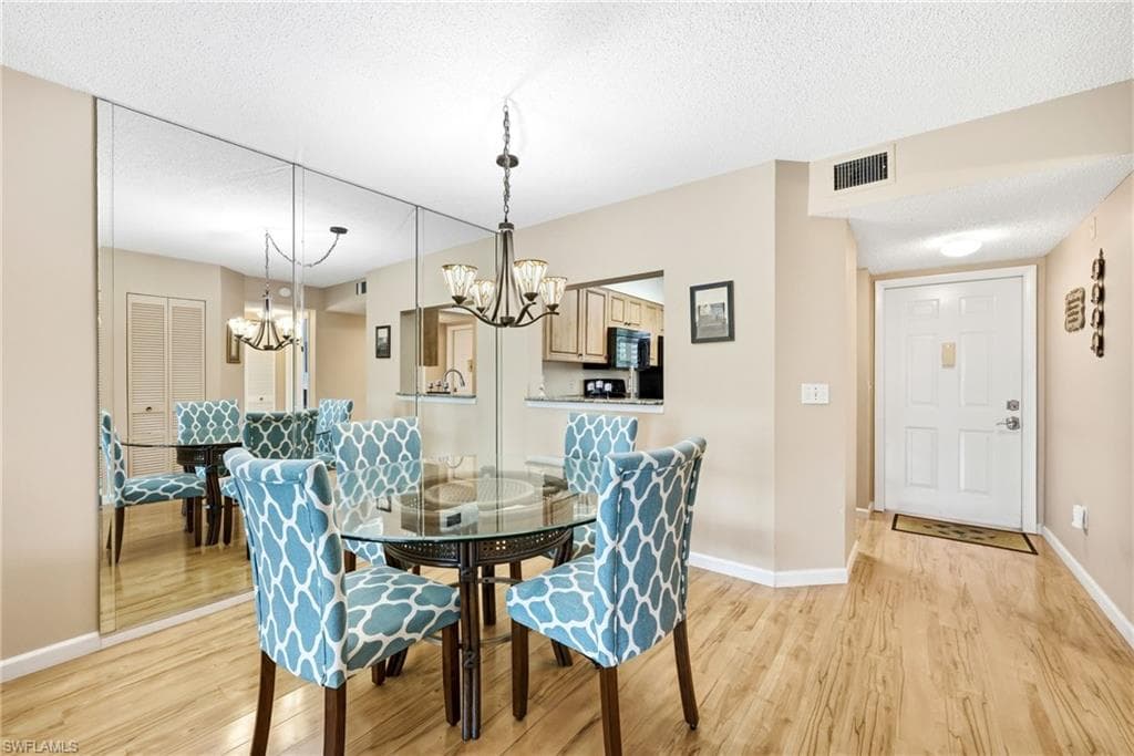 Integrated dining area featuring full-wall mirrored accents, wood-finish flooring, and a decorative chandelier