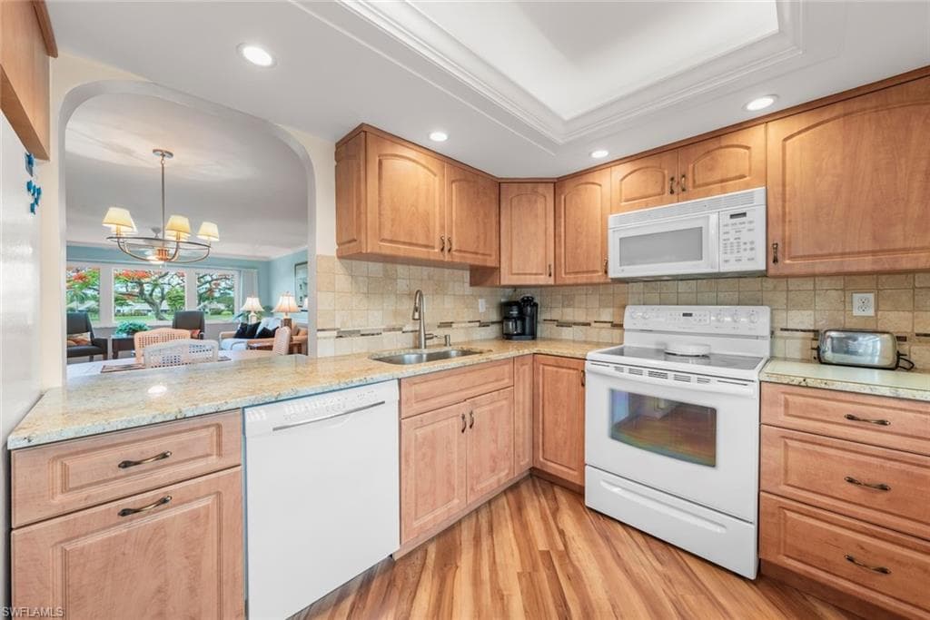 Kitchen featuring laminate flooring, wood cabinetry, a white dishwasher, white electric range, and a built-in white microwave