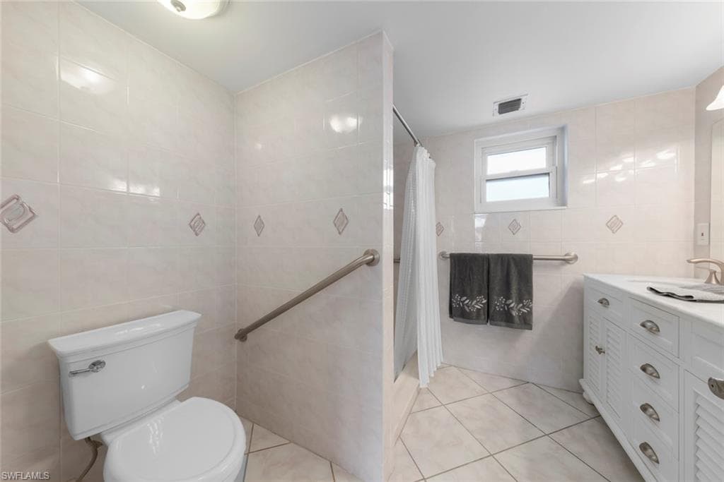 Primary bathroom featuring light-toned tile, a dual vanity with a white countertop and base cabinetry, a window, and a built-in shower area