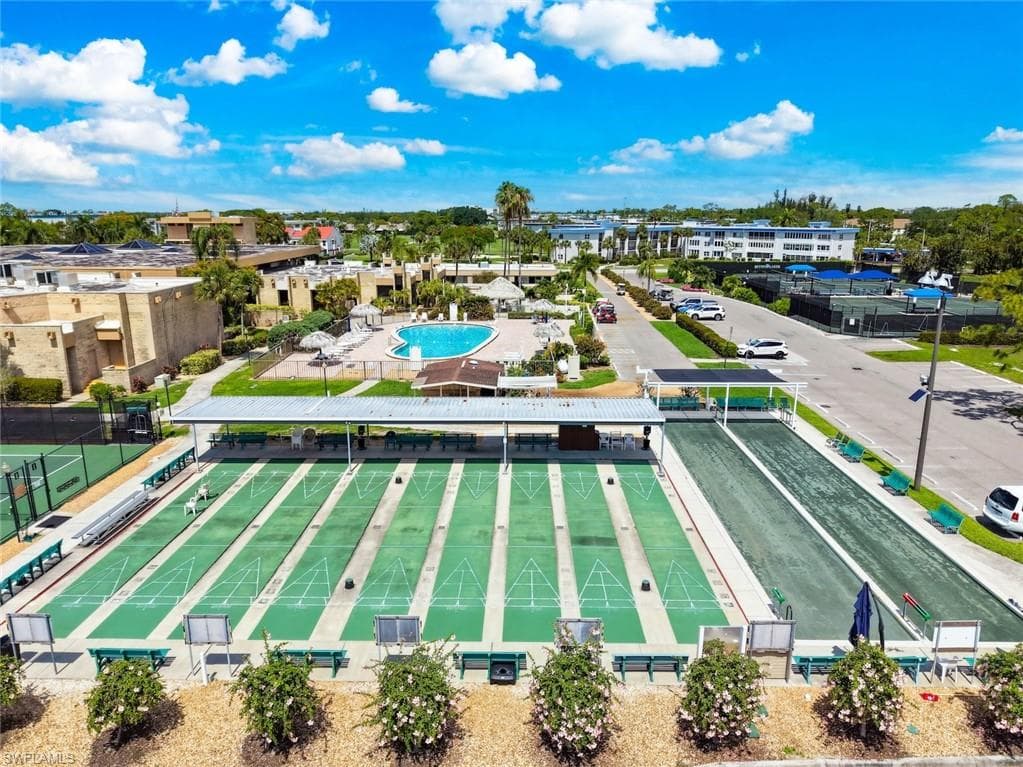 Expansive outdoor recreational area featuring multiple shuffleboard courts, bocce ball, a covered seating area, community swimming pool, pickle ball courts, and tennis courts