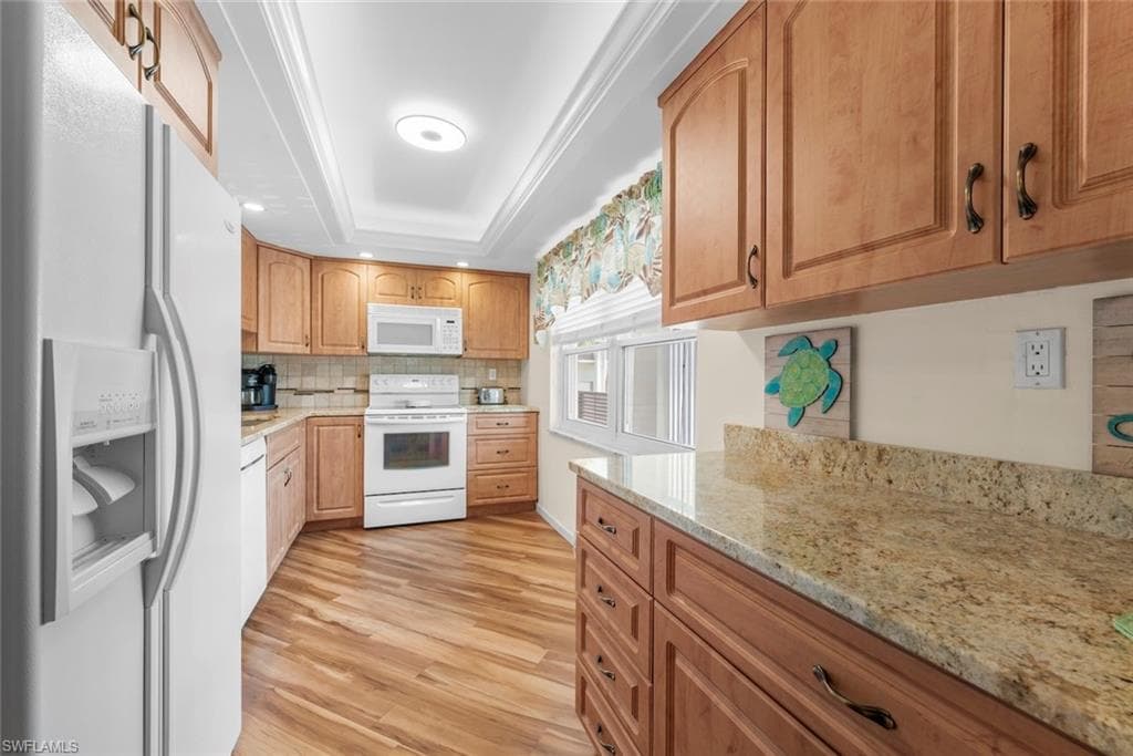 Kitchen featuring laminate flooring, light-toned cabinetry, light-toned countertops, and white appliances