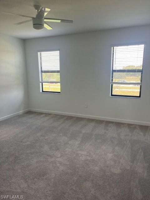 Unfurnished room featuring healthy amount of natural light, dark carpet, and baseboards