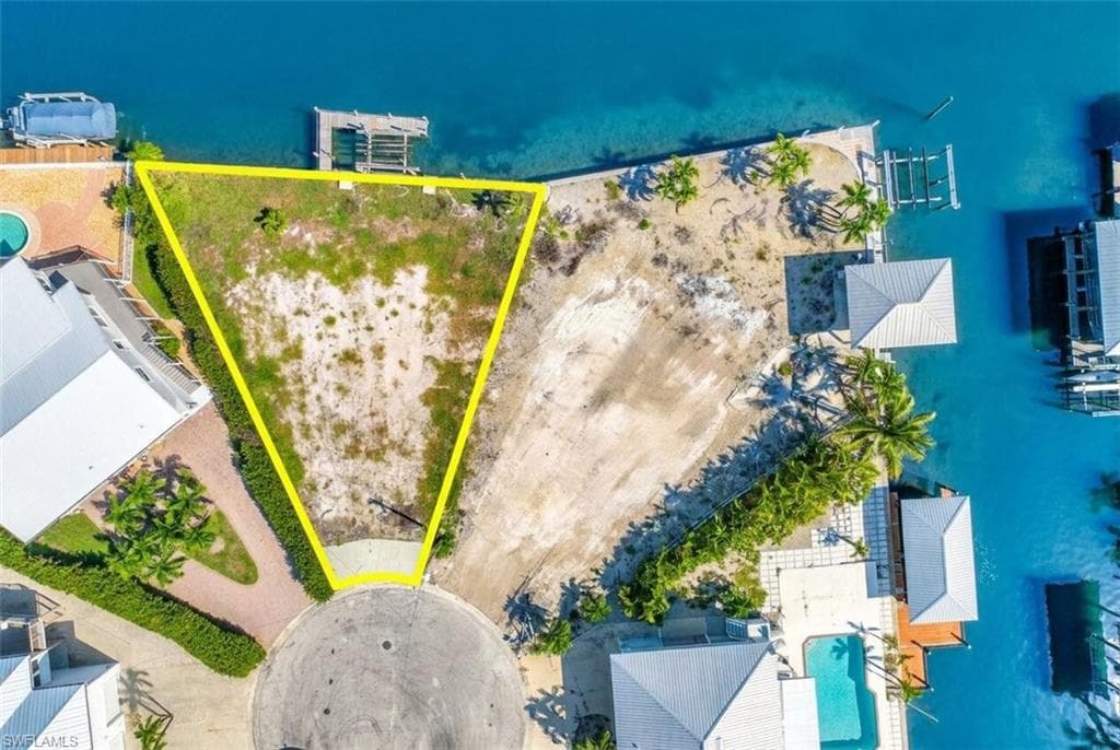 Waterfront lot featuring a cul-de-sac entry, direct water access, and surrounding mature tropical landscaping - Virtually Edited Image