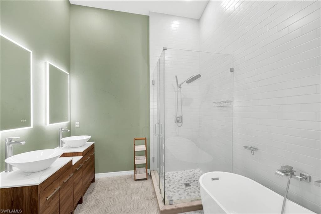 Bathroom featuring a dual vanity with vessel sinks, back-lit mirrors, a frameless glass shower enclosure with a rain shower head, a freestanding soaking tub, and hexagonal floor tiling