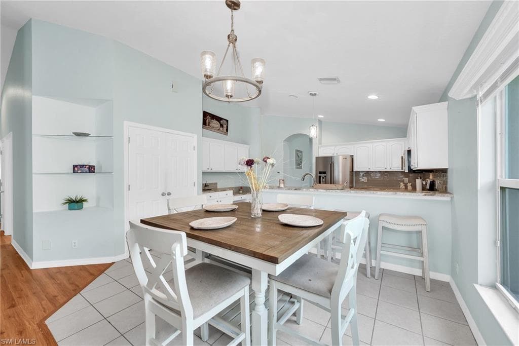 Open-concept dining area featuring a square counter-height table, a chandelier with clear glass shades, and light tile flooring
