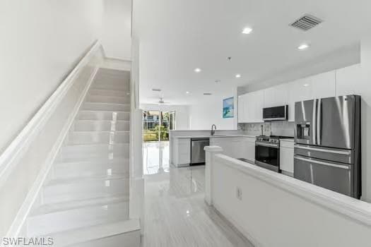 Kitchen with appliances with stainless steel finishes, white cabinetry, recessed lighting, a peninsula, and light countertops