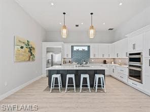 Spacious kitchen featuring an island with seating, white shaker cabinetry, stainless steel double wall ovens, a tile backsplash, and wood-finish flooring