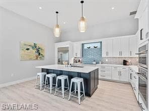 Contemporary kitchen featuring a center island with seating, pendant lighting, light wood-finish flooring, white cabinetry, and stainless steel appliances