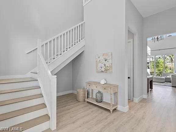 Entryway featuring light wood-finish flooring, a white staircase with carpeted treads, and high ceilings