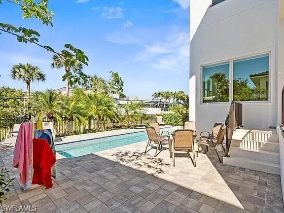 Outdoor living area featuring a rectangular swimming pool, paver patio, and mature tropical landscaping