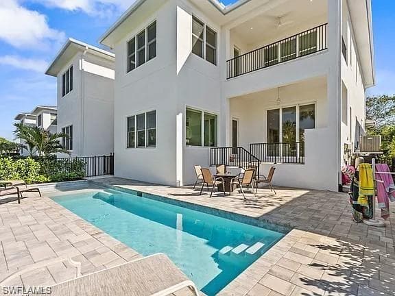 Modern white stucco exterior featuring a private swimming pool, paver patio, second-story covered balcony with black railings, and ground-level covered patio with black railings
