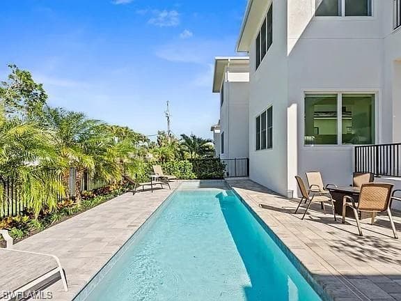 Elongated swimming pool surrounded by a paver patio and lush tropical landscaping