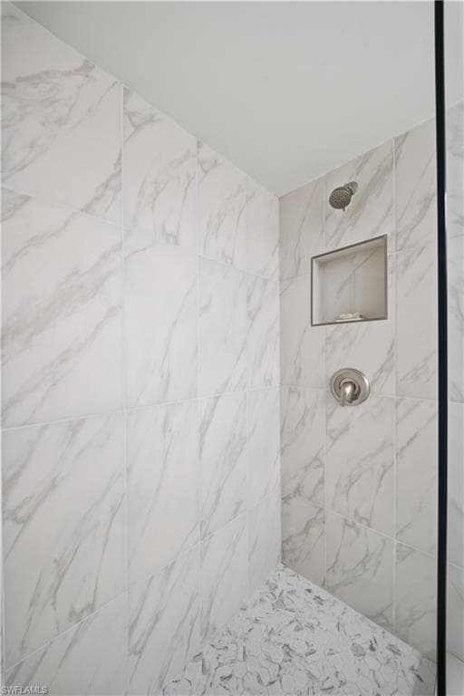 Shower stall featuring large format white tile with grey veining, a built-in shower niche, and a contrasting mosaic tile floor