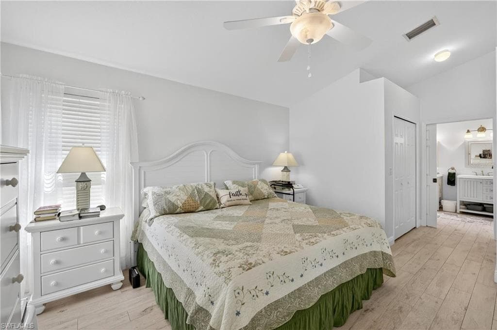 Bright bedroom featuring light wood-finish flooring, a ceiling fan, and a window with white blinds and sheer curtains