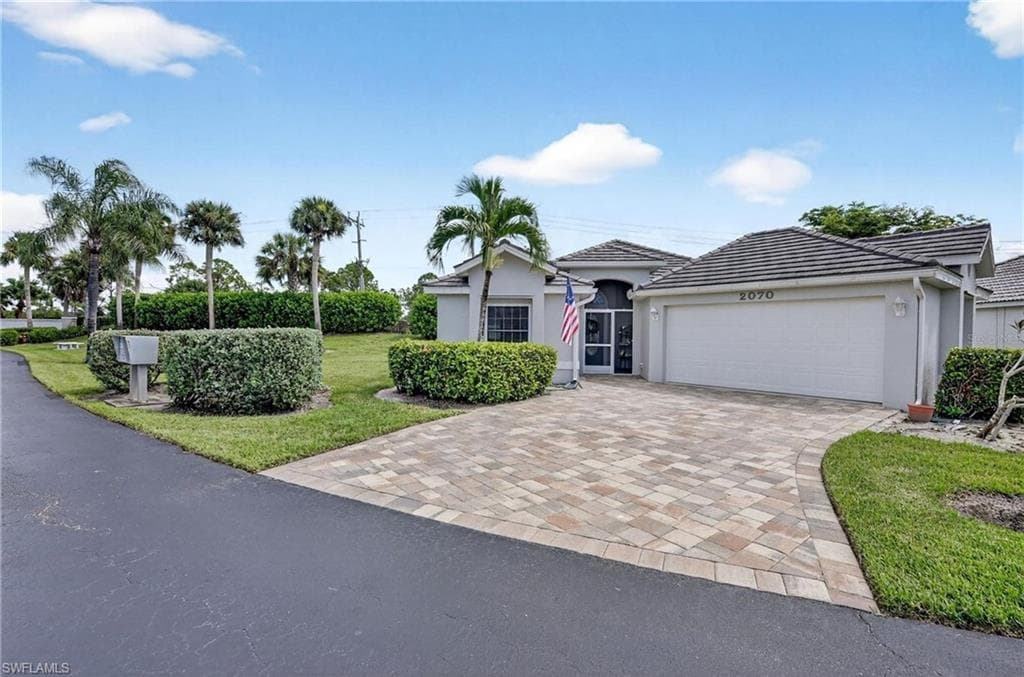 Exterior featuring a paver driveway, an attached garage, a tiled roof, and a screened entry