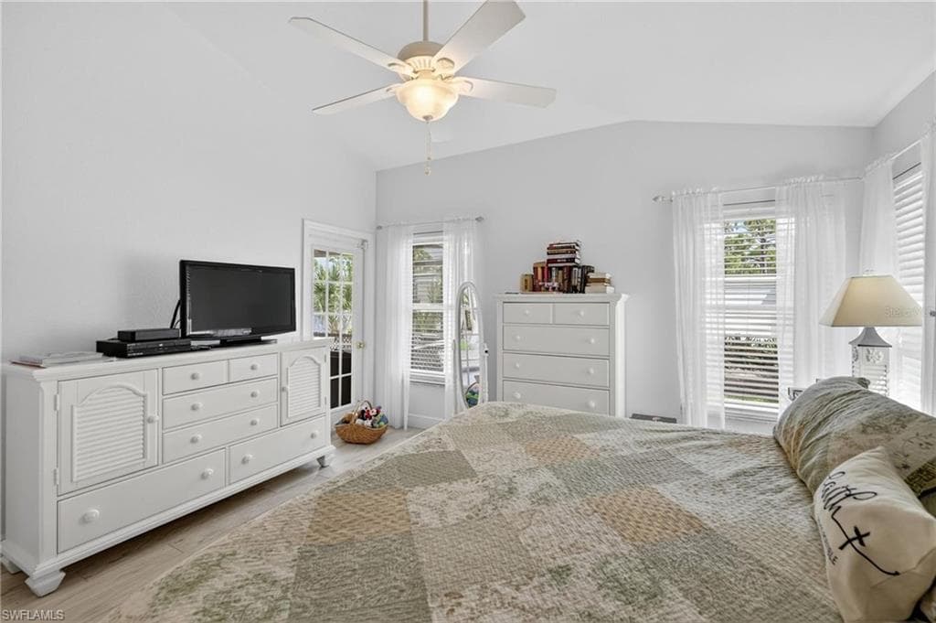 Bright interior room featuring a vaulted ceiling with a ceiling fan, light wood-finish flooring, and multiple windows with blinds